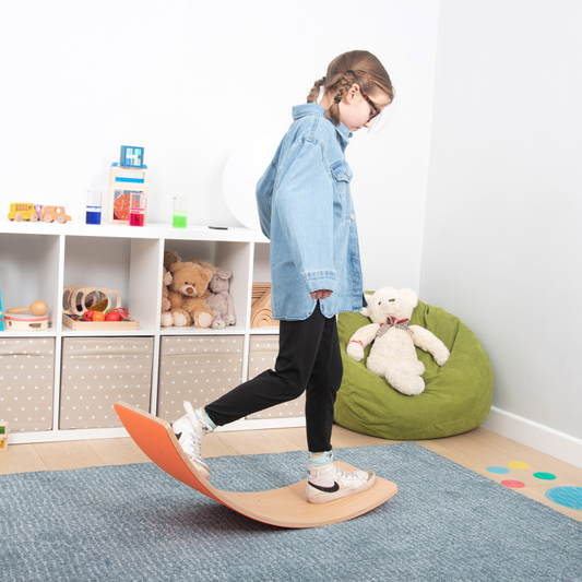 Child standing on a balance board in a room with toys and furniture.