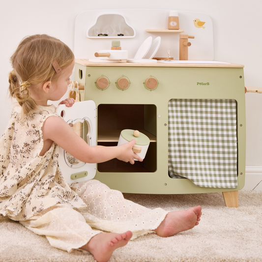 Child playing with a green toy kitchen set on a white floor.