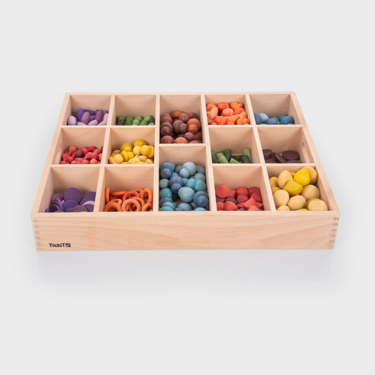 Wooden sorting toy with colourful loose parts in compartments on a white background