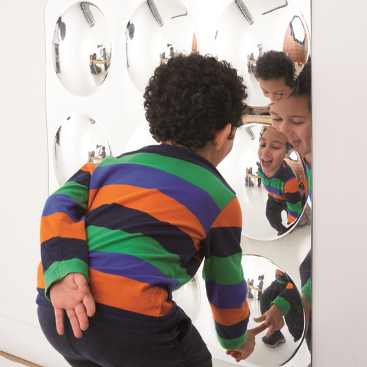 Child in a colourful striped shirt looking at themselves in a mirror with multiple reflective surfaces.
