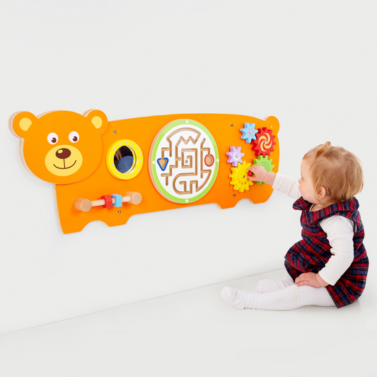 Child playing with a colourful teddy bear-shaped wall panel educational toy on a white background