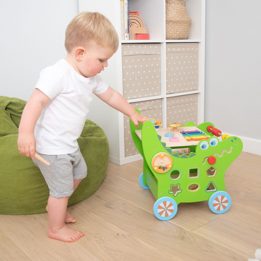 Child pushing crocodile walker in a room.