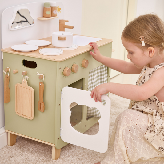 Child playing with a wooden play kitchen set in a home setting.