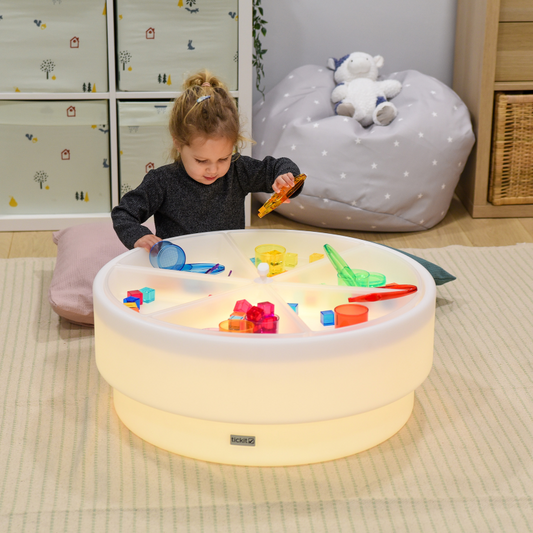 Child playing with toys in a illuminated play table in a room.