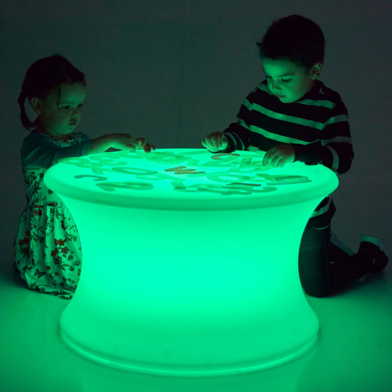 Two children playing with a glowing green table in a dark room.