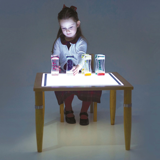 Child sitting at a light table with colourful objects on a dark background