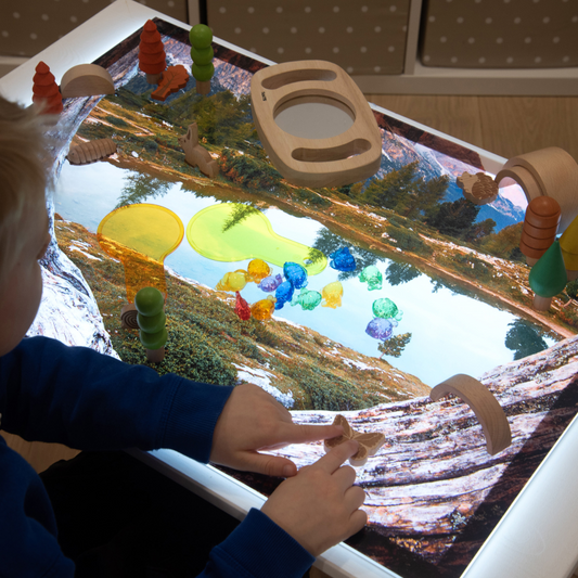 Child playing with sensory toys over a scenic lake playmat on a light panel