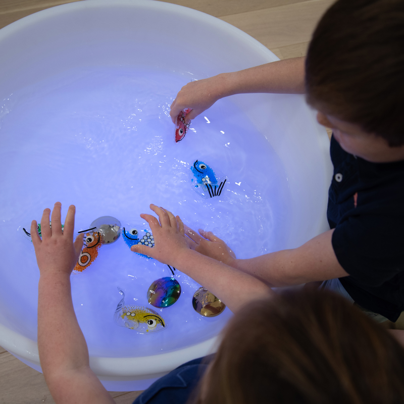 Children playing with colorful toy fish in a glowing water table.