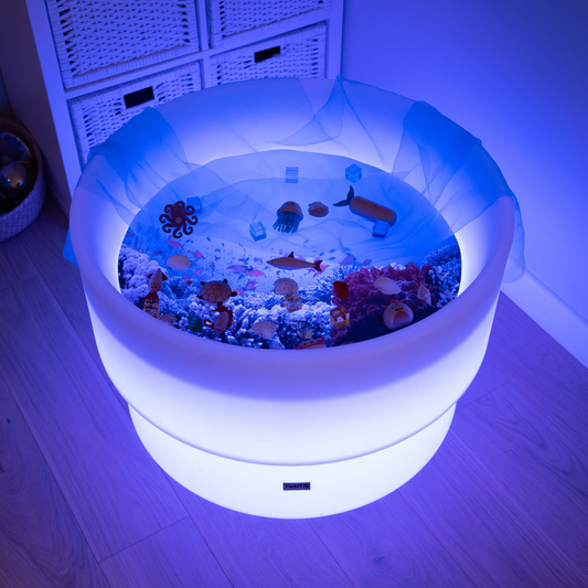 Sensory  light play table with a sealife play mat  with a sensory scarf and toy set up on it.