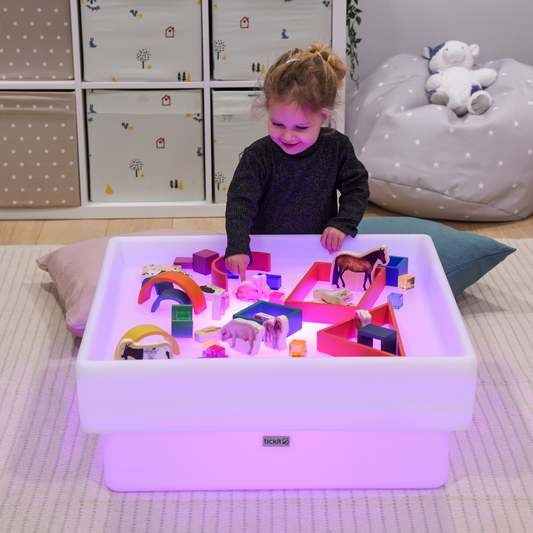 Child playing with colorful toys on a light-up table in a child's room.