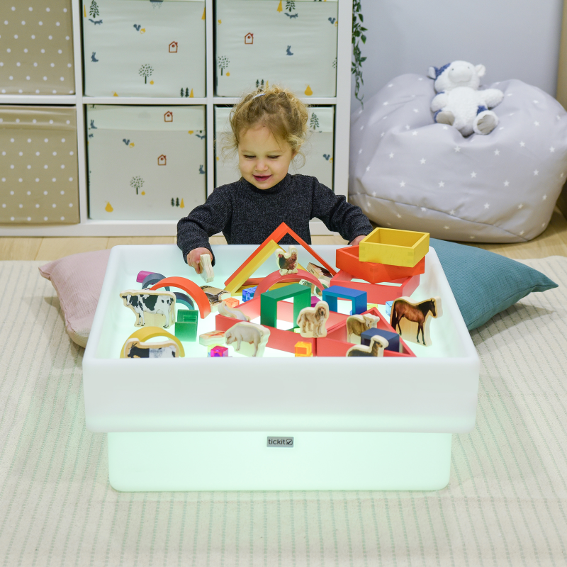 Child playing with a colorful toy set on a light-up table in a room.