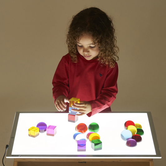 Child playing with colorful blocks on a light-up table against a plain background
