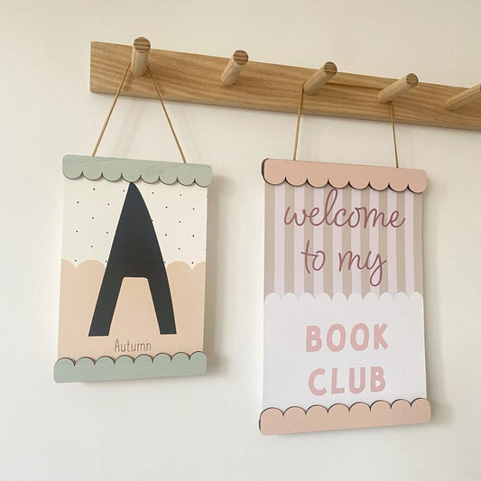 Two decorative signs hanging on a wooden rod against a white wall.