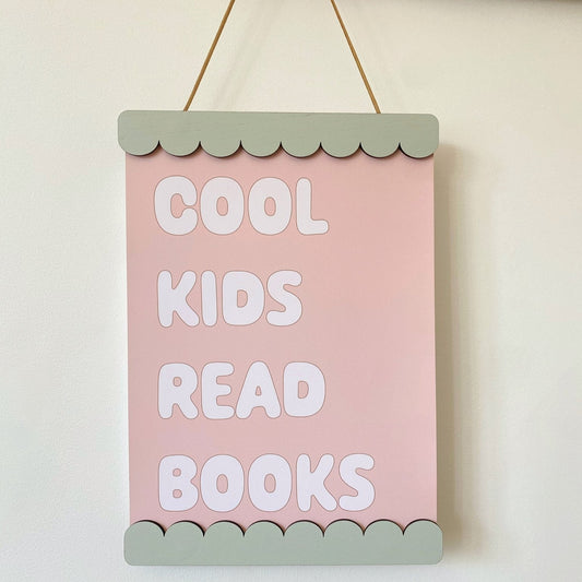 Pink sign with 'Cool kids read books' text on a white wall
