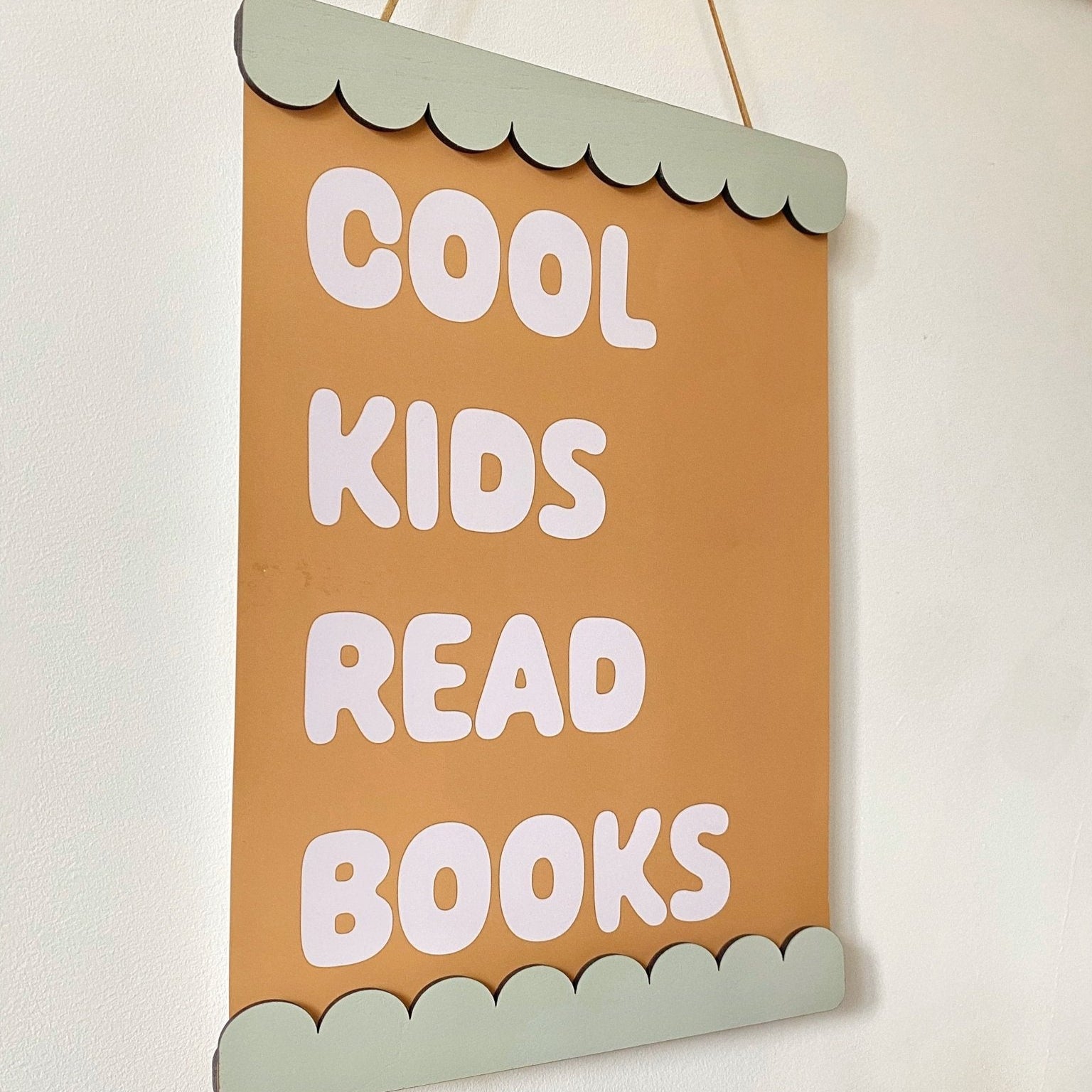 Decorative sign with 'Cool kids read books' text on a plain background