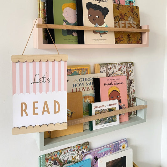Children's books on a shelf with a 'Let's Read' sign against a white wall.