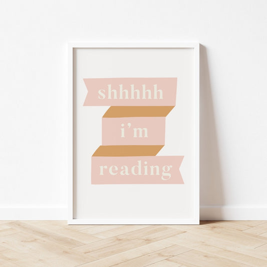 Framed print with 'shhhhh i'm reading' text on a white wall.