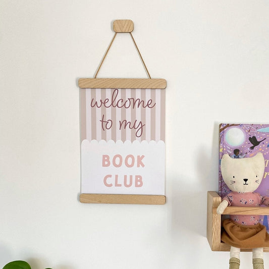 Children's bookshelf with books and a sign that reads 'welcome to my Book Club' on a white wall.