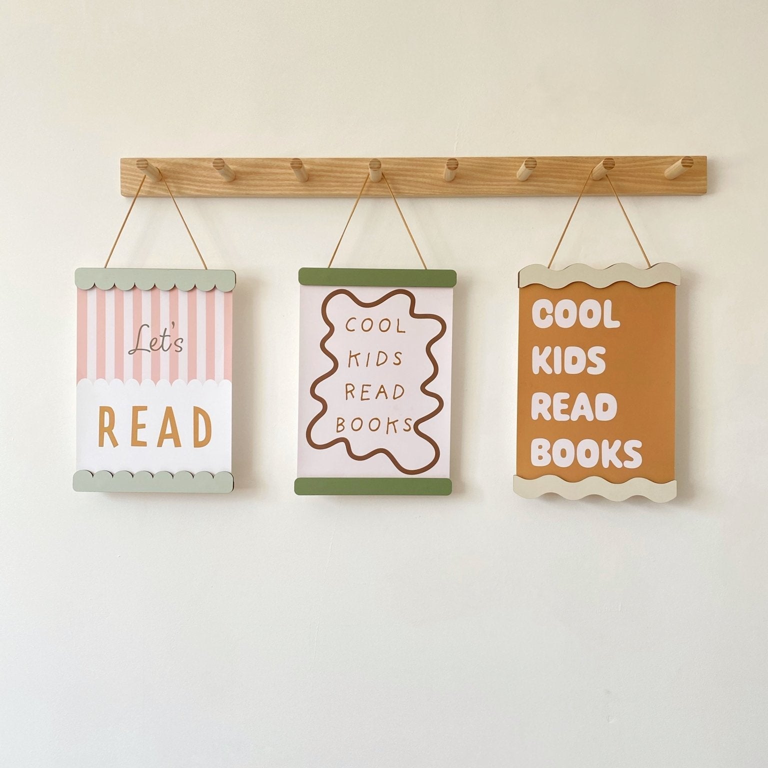 Three motivational signs for children hanging on a wooden rod against a white wall.