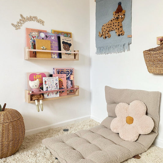 Children's room with a beige floor pillow, wall hanging, and shelves.
