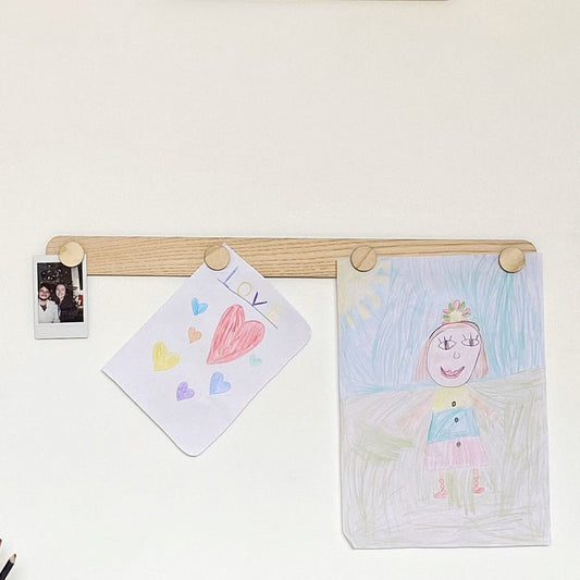 Children's drawings on a wooden peg board against a white wall.