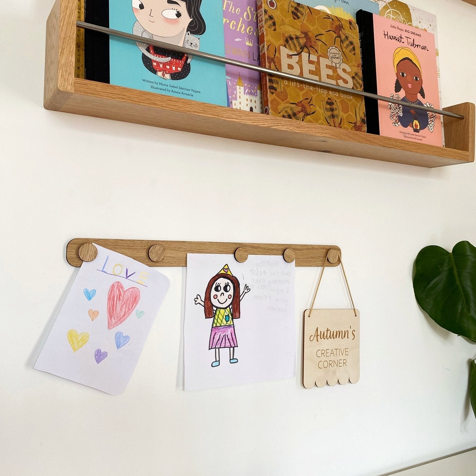 Wooden shelf with children's books and a wall-mounted board with drawings and a sign.