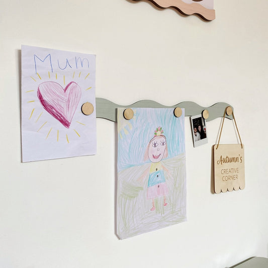 Children's artwork and notes displayed on a magnetic board with wooden pegs.
