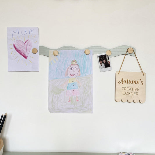 Children's artwork and a sign on a magnetic board against a white wall.