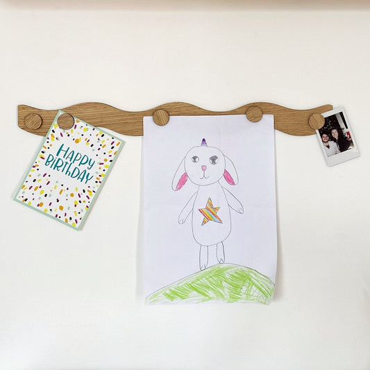 Wooden peg board with children's artwork and a card on a white background