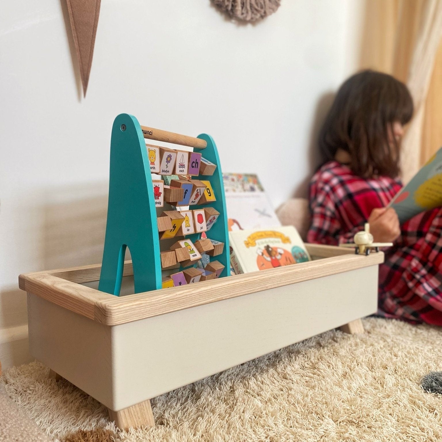 Children's toy storage box with wooden toys on a carpeted floor.