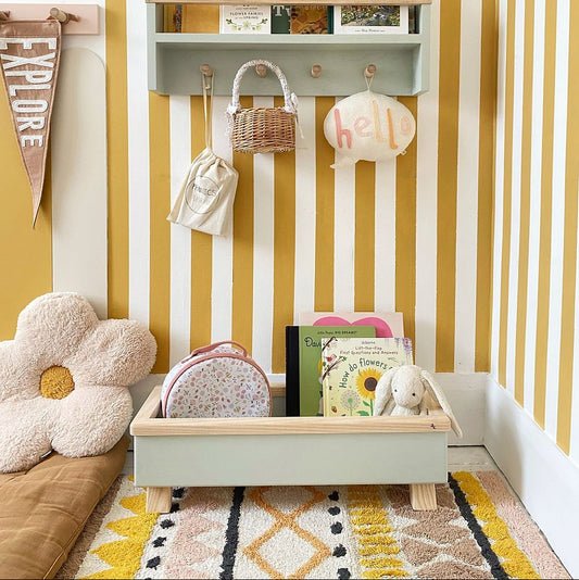 Children's room with yellow and white striped wall, shelves with books and toys, and a colorful rug.