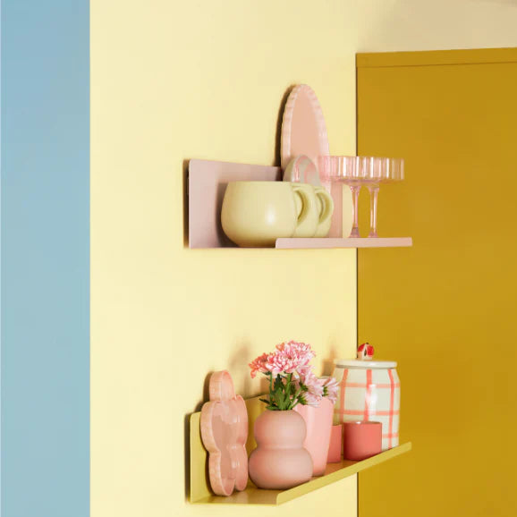 Decorative shelves with pink and yellow items against a multicolored wall.