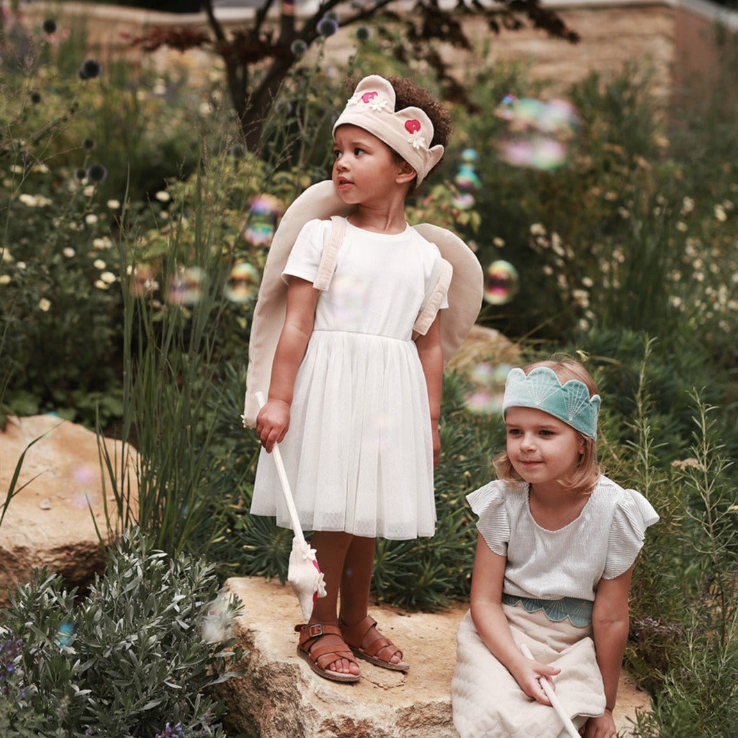 Two young girls in dresses and headbands standing in a garden setting.