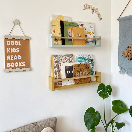 Children's books on a wall-mounted shelf with decorative signs in a room setting.