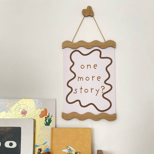Wooden shelf with books and a sign reading 'one more story?' on a white wall.