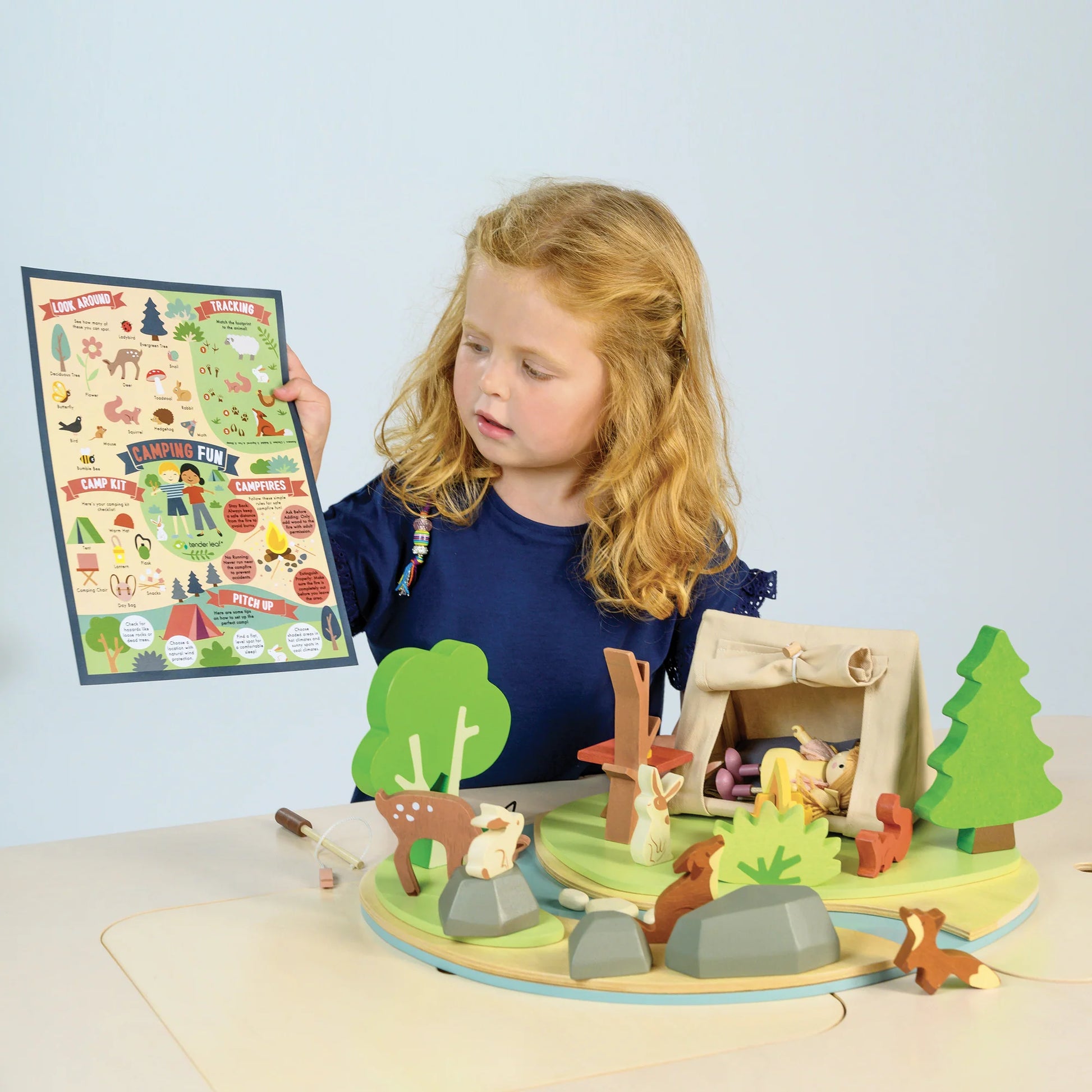Child playing with a wooden forest scene toy set on a light blue background