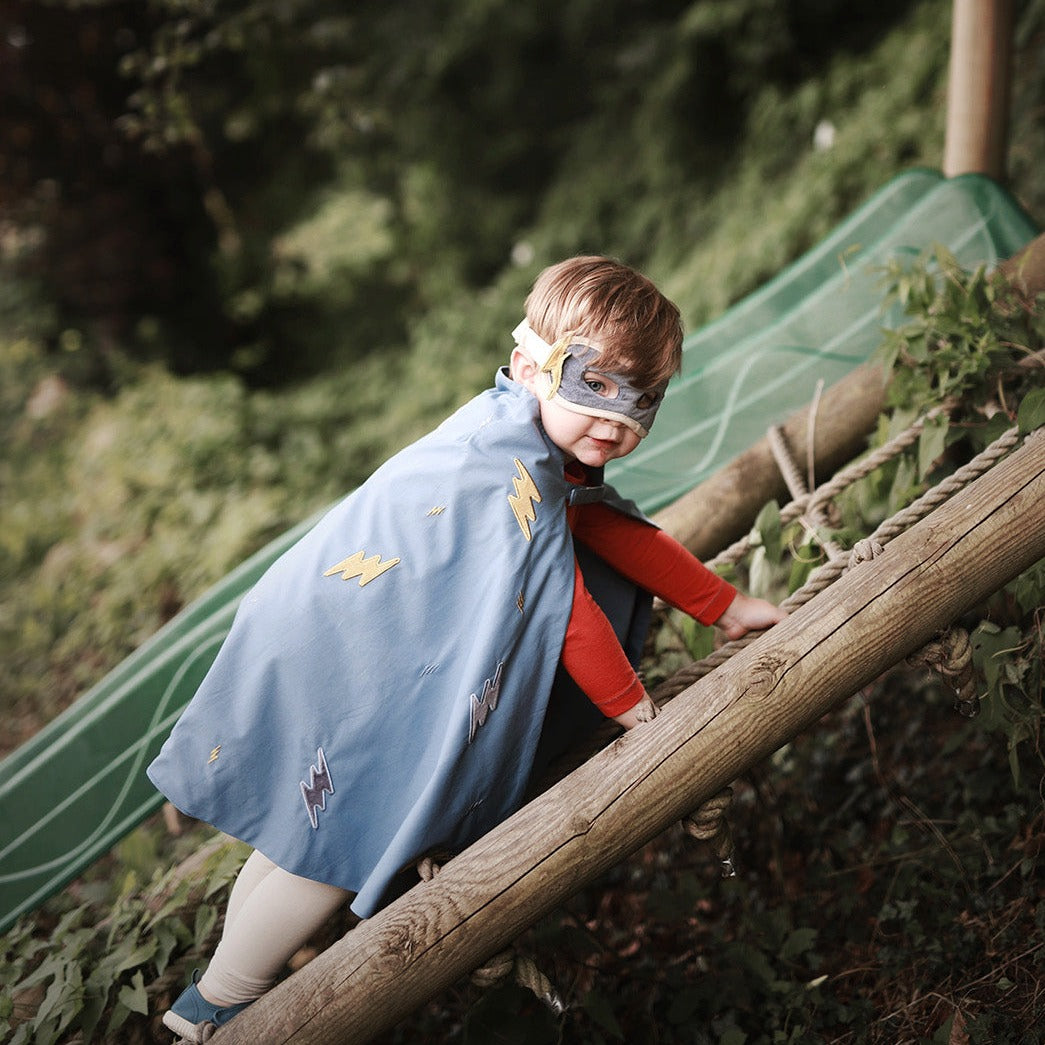 Child in superhero costume climbing a log outdoors